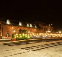 Zdjęcie ilustruje przejazdy koleją wąskotorową w Pleszewie - skałd z podświetleniem świątecznym