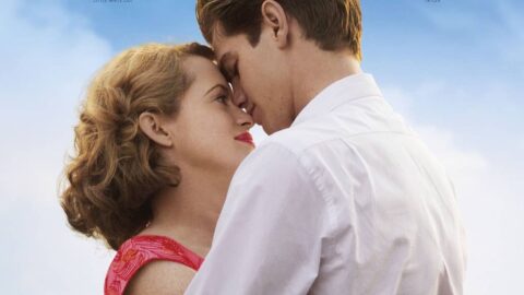 Zdjęcie przedstawia dwójkę głównych aktorów wystepujących w filmie pt. "PEŁNIA ŻYCIA". Aktorzy Andrew Garfield oraz Claire Foy stoją przytuleni do siebie, patrząc sobie w oczy. Ona ubrana jest w czerwoną sukienkę a On w białą koszulę i niebieskie spodnie.